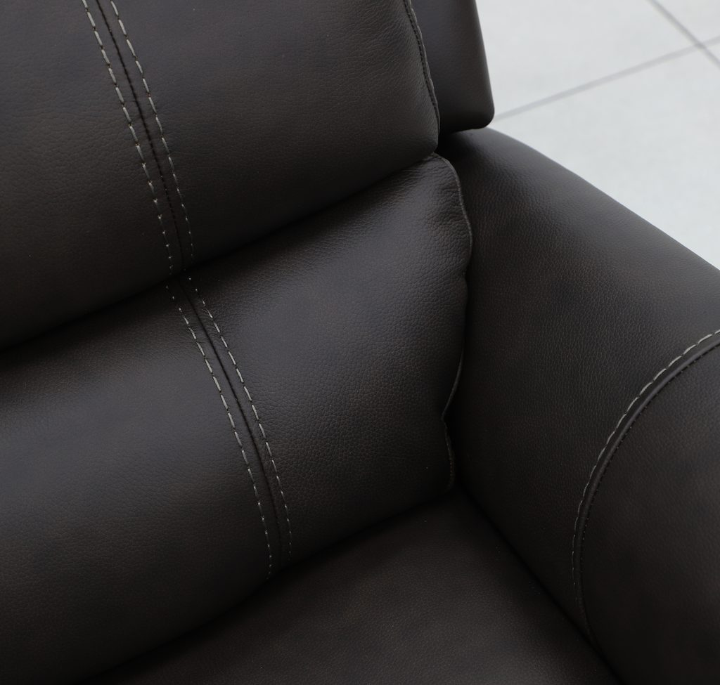 Close-up of contrast double topstitching along the seat and arm of a dark leather recliner.