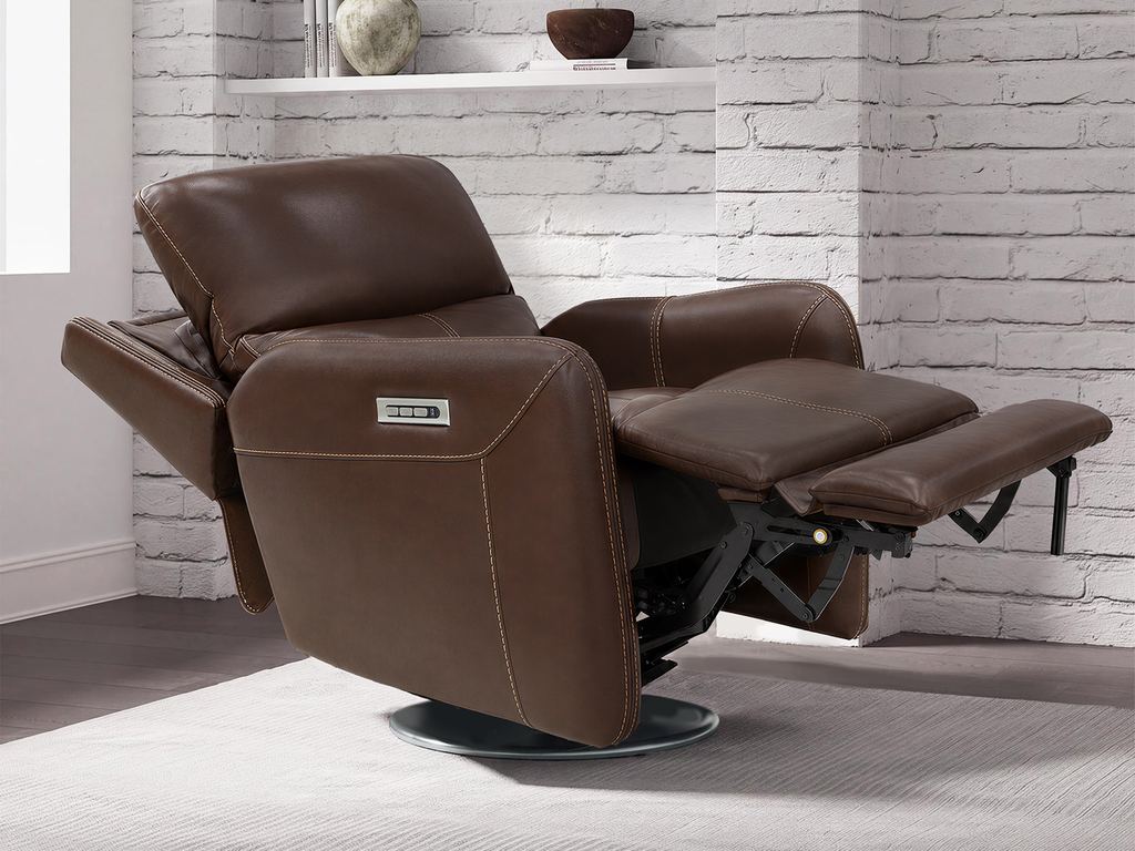 A brown leather swivel glider fully reclined, footrest raised and headrest tilted forward, in front of a white brick wall.