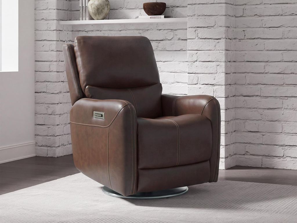 A brown leather swivel glider recliner on a round polished base, in front of a white brick wall with open shelving.
