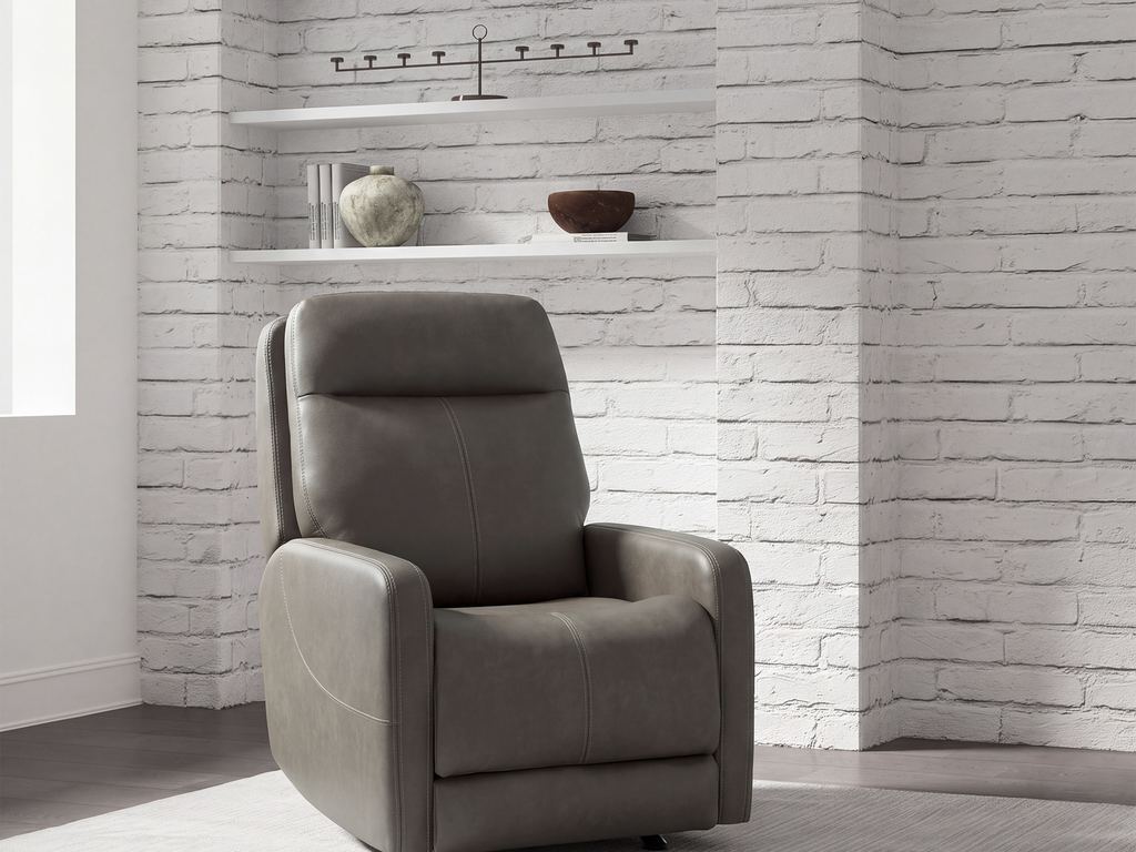 A gray leather power recliner in front of a white brick wall with open shelving and framed prints.