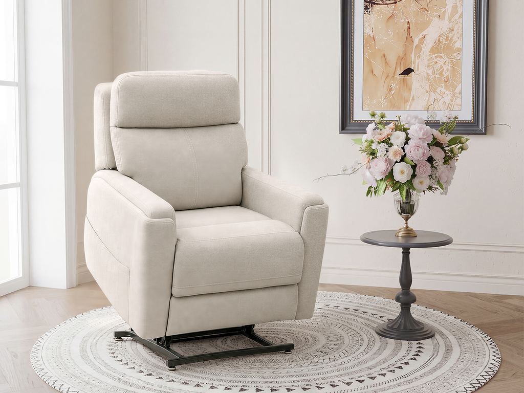 A cream fabric power lift chair raised and tilted forward into its standing-assist position, on a round woven rug beside a pedestal table.