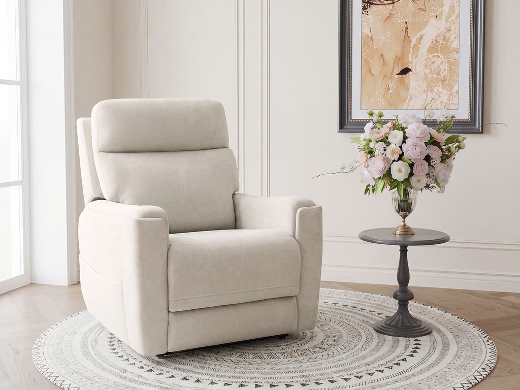 A cream fabric power lift chair on a round woven rug, beside a pedestal table with flowers and a framed print.
